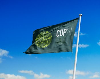 Green flag featuring the COP28 logo flutters in the wind against a blue sky